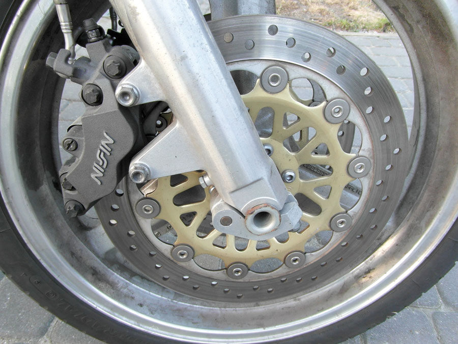 Symetryczny czterotłoczkowy zacisk hamulcowy NISSIN, zamontowany na goleni zawieszenia przedniego w motocyklu Honda CB 1000 Big One 